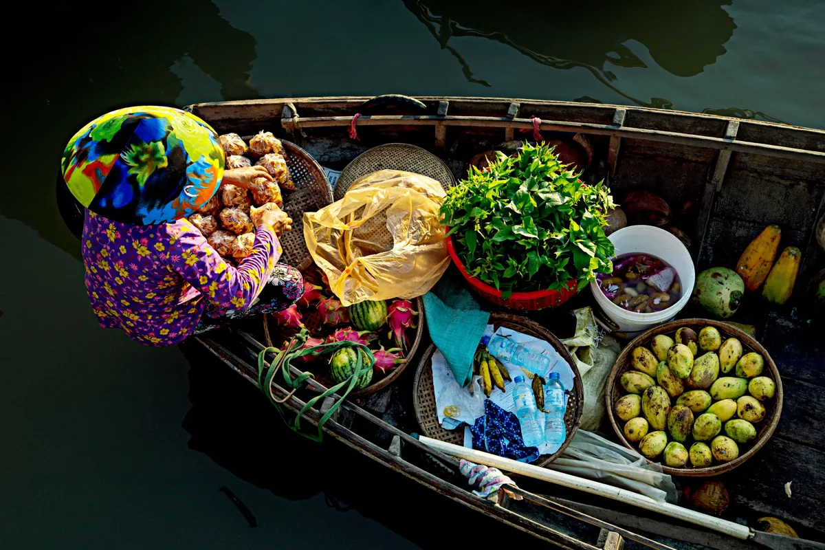 A vibrant view of a vendor in a traditional floating market selling fresh fruits and vegetables from a boat. (Source: Tuấn Nguyễn Văn)